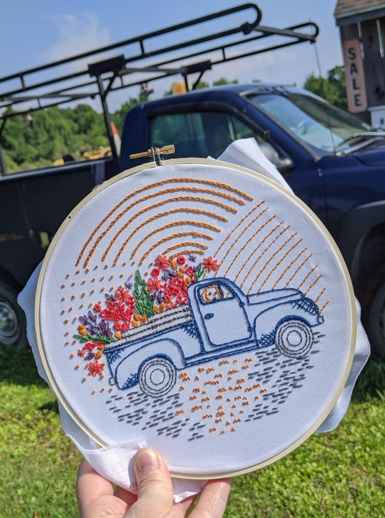 embroidery hoop art with vintage truck, flowers and a dog, pictured in front of a n old truck