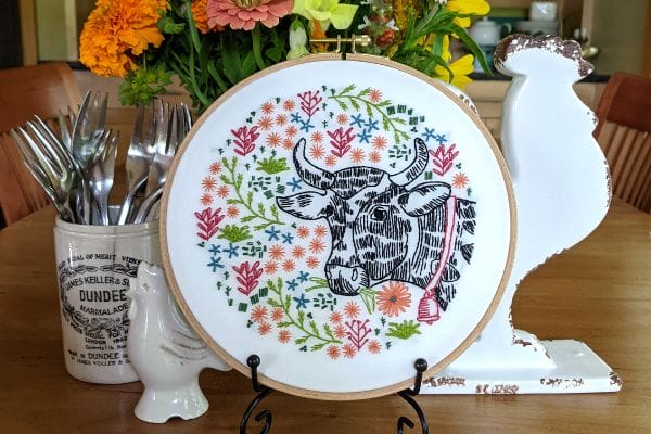 Embroidered cow hoop-art displayed on summer table with flowers