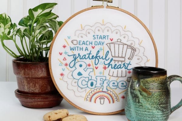 Coffee-inspired embroidery kit displayed alongside plant and mug on side table
