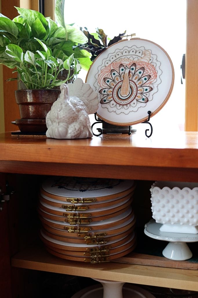 embroidery hoop art with harvest table turkey displayed on buffet alongside house plants and thanksgiving-themed decor