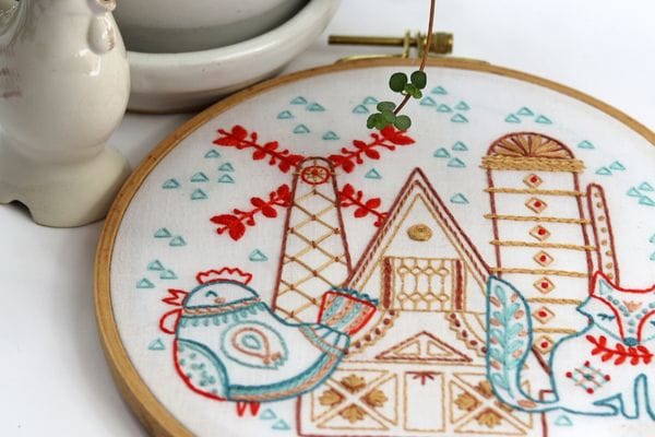 embroidery project with folk art hen and fox in front of old Dutch farm with windmill