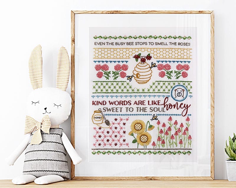 Framed honeybee embroidery sampler displayed in a nursery.