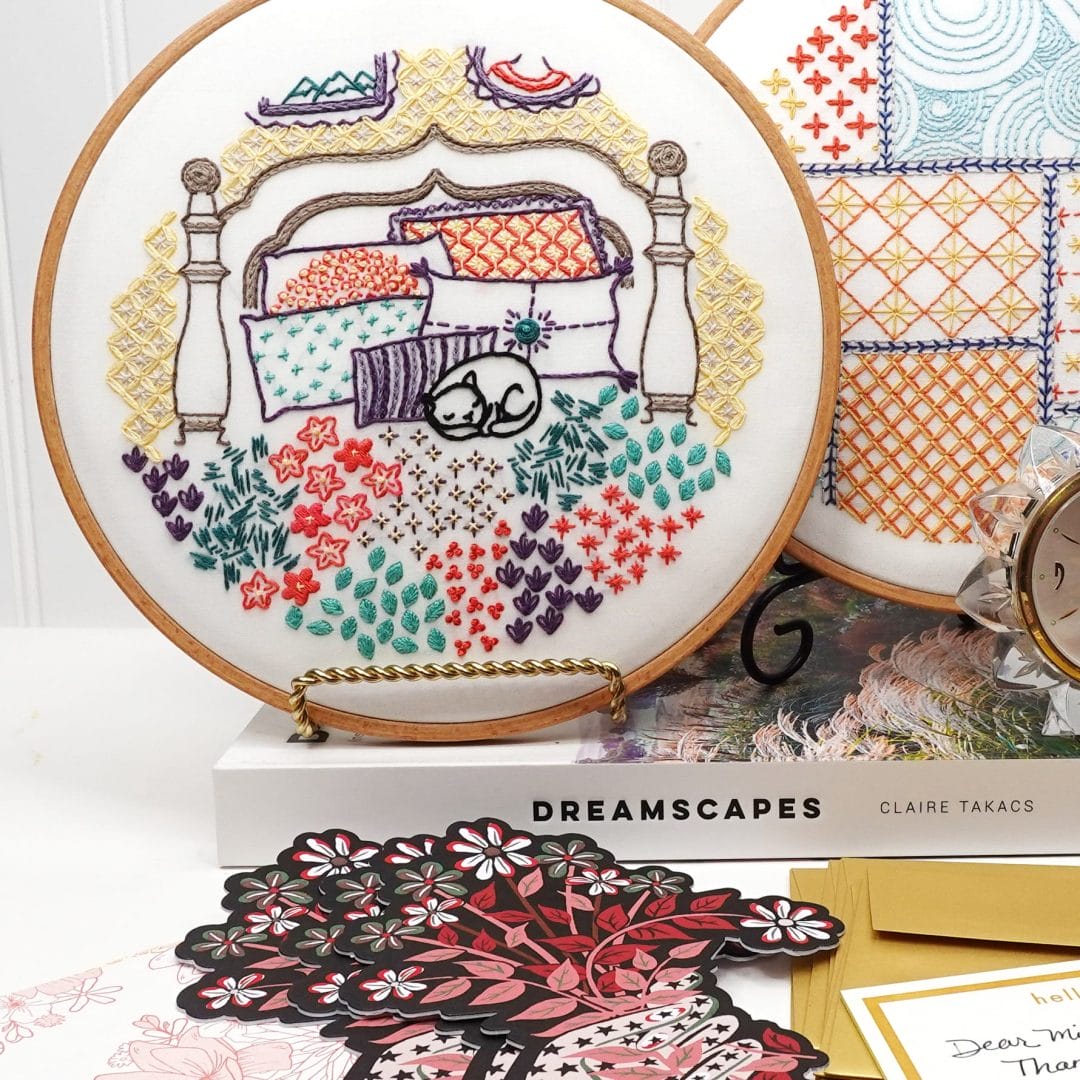 Home-themed embroidery hoop art with cat napping on bed.